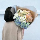 A person in a beige shirt holds a bouquet of colorful hydrangeas and white daisies.