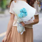 A bouquet of four bright blue roses, wrapped in light green and white paper, with a silver ribbon.