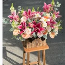 Pink lilies, roses, and anthurium flowers in a rustic wooden box on a stool.