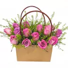 Basket of pink and purple roses with green filler flowers and a brown handle.