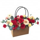Basket of red roses, gerbera daisies, and carnations in a brown paper bag.