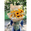 Bouquet of sunflowers and baby's breath flowers wrapped in brown paper and green fabric.