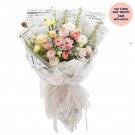 Bouquet of pink and yellow roses and lisianthus wrapped in newspaper and white mesh.