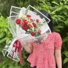 Woman in red floral top holding a bouquet of red ranunculus and white tana flowers.
