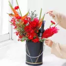 Red flowers with a bottle of red wine in a black vase with gold accents.