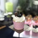 Pink polka dot cupcake with whipped cream, blueberry, chocolate, and cookie pieces.