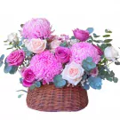 Pink and purple chrysanthemums and roses in a woven basket.