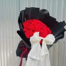 A luxurious bouquet of 50 red roses wrapped in black paper with a sheer white bow.
