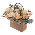 Peach roses, gerbera daisies, and carnations in a cardboard gift bag with black handles.
