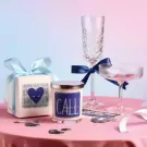 Gift set with scented candle and champagne glasses on a pink tablecloth.