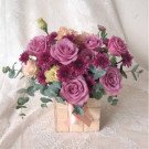 Box of purple roses, carnations, and chrysanthemums with eucalyptus leaves.