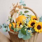 Basket of sunflowers, oranges, and eucalyptus with a golden bow.