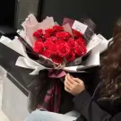 A bouquet of red roses with delicate pearl strands, wrapped in black and white paper.