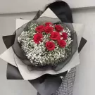 A bouquet of red roses and baby's breath flowers wrapped in black and white paper.