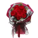 A bouquet of red Ohara roses with greenery, wrapped in pink and gray paper, tied with a black ribbon.