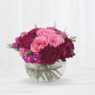 Pink roses and deep purple carnations in a clear glass bowl.