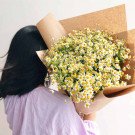 Bouquet of white and yellow chamomile flowers wrapped in brown paper, held by a person.