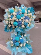 Two blue and white floral arrangements with blue monstera leaves.