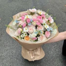 Pink and white roses and carnations with small blue and white flowers in brown paper wrap.