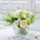A round glass vase filled with white and green flowers and greenery.