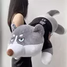A person holds a large gray husky plush toy wearing a black shirt with white lettering.