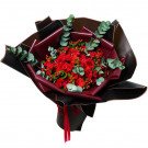 A bouquet of red roses and carnations with eucalyptus and red berries, wrapped in black and burgundy paper.