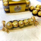 Ferrero Rocher chocolates in a gift box and a clear wrapper tied with a gold ribbon.