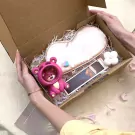 Gift box with a pink bear, eye mask, small photo, and white flower-shaped candle.