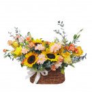 A woven basket arrangement of sunflowers, roses, gerbera daisies, and other yellow and orange flowers.