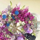 Purple and pink floral arrangement with orchids and anthuriums, featuring blue decorative accents.