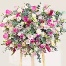Large flower stand with pink and white roses, gerbera daisies, and filler flowers on a light background.