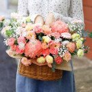 Pink and yellow flowers in a woven basket, held by a person in a floral shirt.