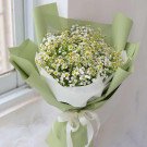 Bouquet of small white and yellow daisies with baby's breath, wrapped in light green paper and tied with a white ribbon.