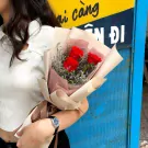 Three red roses in a bouquet wrapped in paper, held by a person wearing a white top and watch.