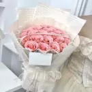 A glamorous bouquet of pink roses wrapped in white paper and tied with a ribbon.