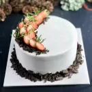 White frosted cake adorned with sliced strawberries, greenery, and chocolate shavings.