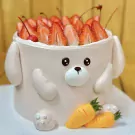Strawberry bunny cake topped with sliced strawberries and cherries, with fondant carrots at the base.