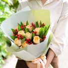 Bouquet of peach roses with red berries and green leaves, wrapped in pale green and white paper.