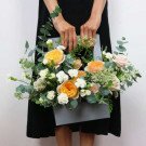 Orange and white flowers in a gray box, held by a person in a black dress.