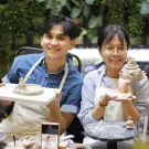 Couple smiling and holding clay creations at a pottery workshop.