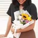 Woman holding a bouquet with a sunflower, roses, and a yellow stuffed dog.
