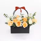 Orange and white roses in a black basket with a red bow.