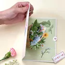 A hand opens a pop-up card showing a vibrant bouquet of flowers.