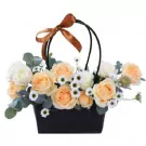 A basket of peach roses, white roses, and daisies with eucalyptus leaves, tied with a brown ribbon.