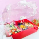 Red gift basket with cakes and fresh fruits, decorated with a crown and flowers.