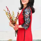 Woman in red dress holding yellow and red pussy willow branches with a red lucky charm.