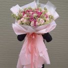 A large bouquet of pink and white roses with green accents, wrapped in pink paper and tied with pink ribbons.