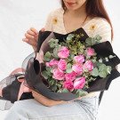 Woman holding a bouquet of pink roses and eucalyptus leaves wrapped in black paper.