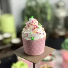 A pink polka-dot cupcake with white frosting, red and green sprinkles, and green stars.