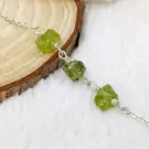Silver bracelet with rough green stones on a wooden surface.